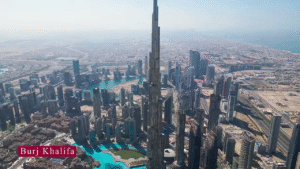 Aerial view of the Burj Khalifa skyscraper towering over the Dubai city skyline, featured in the 2025 UAE Travel Guide, surrounded by modern buildings and blue artificial lakes under a clear sky.